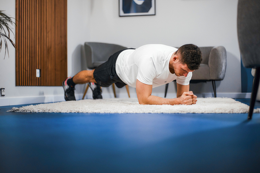 Homme coach FizzUp en position de gainage planche sur avant-bras dans son salon en suivant son programme abdominaux
