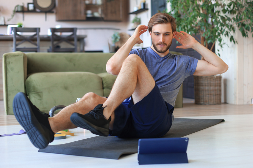 Homme en train de faire des twists dans son salon sur son tapis de fitness en suivant son programme de musculation à la maison sur son application FizzUp sur sa tablette