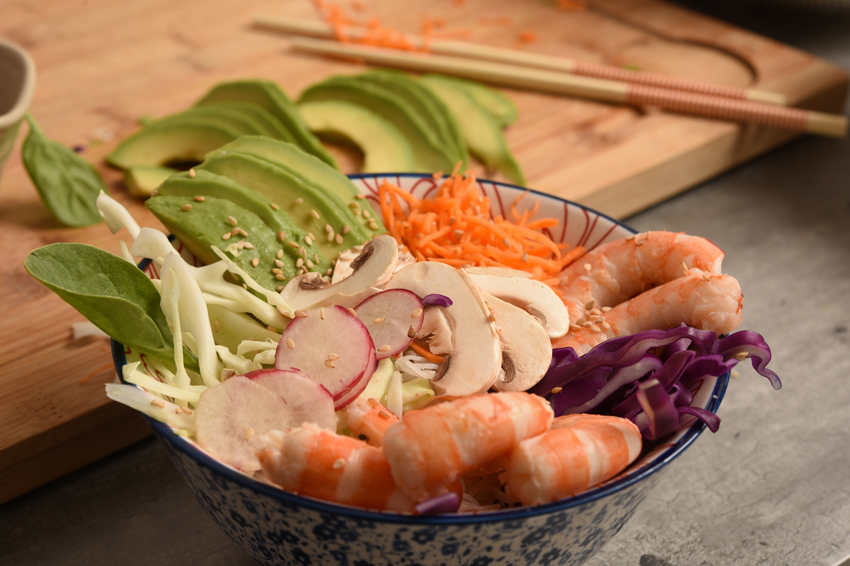 Photo d'une recette healthy avec des radis, de l'avocat, des crevettes, des carottes, du choux rouge et du choux blanc dans un bol