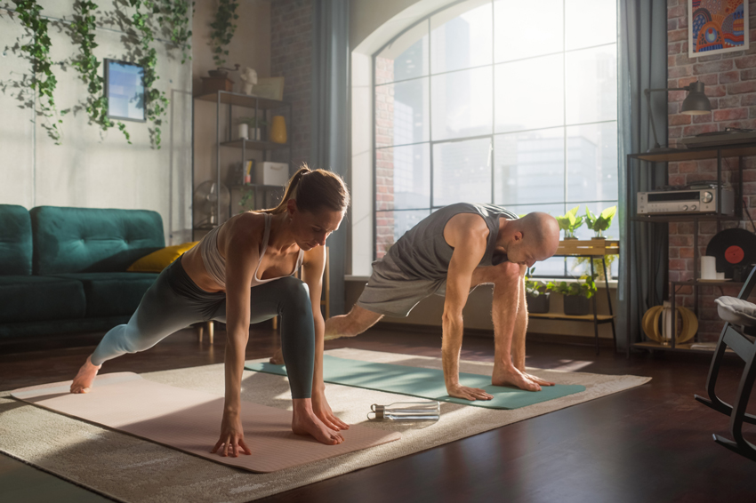 Un homme et une femme faisant du sport à la maison dans leur salon sur leur tapis de fitness 