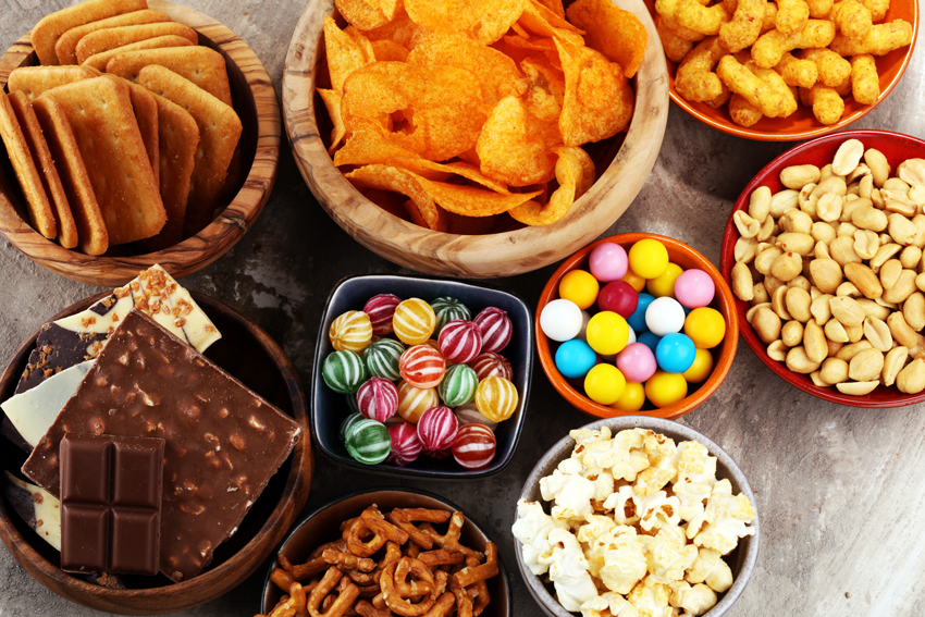 Plusieurs assiettes et récipients de nourritures grasses et sucrées : chips, cacahuètes, biscuits salés, popcorn, bombons et chocolats.