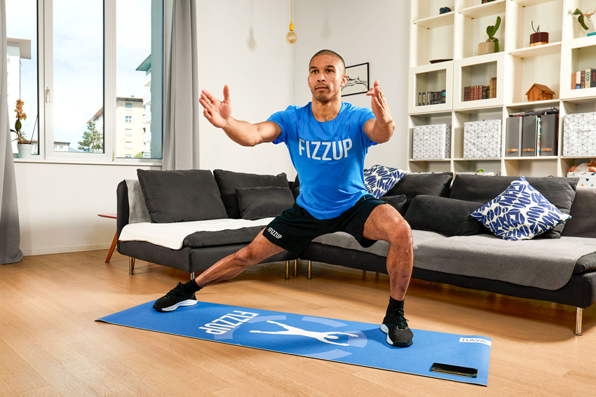 Coach sportif faisant une fente sur un tapis dans un salon.