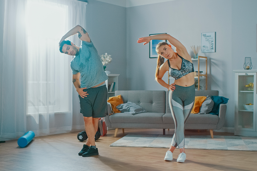 Un homme et une femme, en tenue de sport en train d'effectuer des étirements dans leur salon.